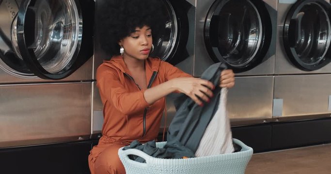 African American young woman sorting laundry in basket sorting clothes before washing sitting in the self-service public laundry.