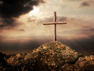 close up wooden cross on rocky hill over sunset sky
