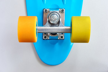 Detail of blue plastic mini cruiser penny board or skate board with yellow and orange wheels and metal attachment on light grey background with copy space. Back view in soft light 