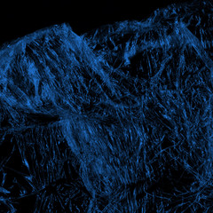 Transparent blue plastic wrap on the black background. Plastic shopping bag texture. Reusable trash and waste.