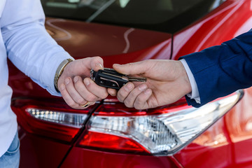 Male hand with car keys against new car in showroom