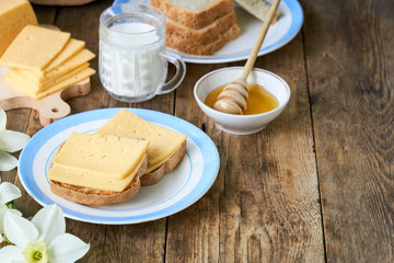 Breakfast with cheese sandwich, milk and honey on a wooden table