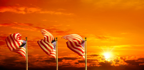 Conceptual image of waving American flags at tall poles in a row over orange colored sunset sky