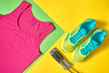 Sport shoes, female top bra and skipping rope on colorful yellow and green backgroundon, copy space. Top view, flat lay. Healthy lifestyle concept, overhead shot