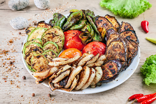 Close up view on grilled vegetables on white plate served on white wooden table. tomato, pepper, eggplant, zucchini and onion cooked over charcoal. Copy space, picture for barbecue. Healthy food