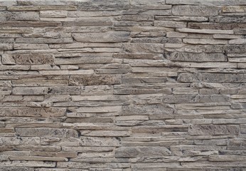 Stone cladding wall made of  striped stacked slabs of natural brown rocks stained with black .
