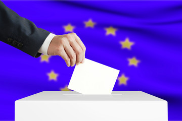 Man putting a ballot into a voting box with European Union flag on background.