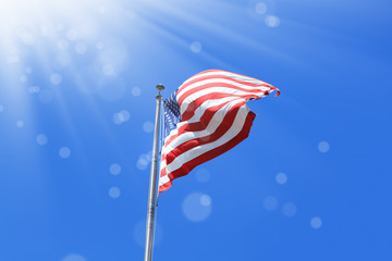 Conceptual image of waving American flag over sunny blue sky