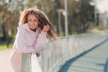 Young happy attractive woman posing on a fence near a running track