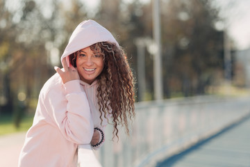 Young happy attractive woman posing on a fence near a running track