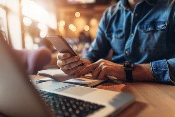 Close up of young man hand texting massage on phone while sitting at cafe.