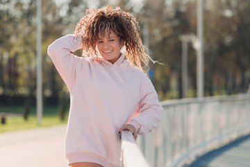 Young happy attractive woman posing on a fence near a running track