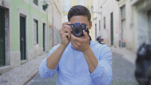 Focused young photographer taking pictures on street. Handsome brunet man with photo camera outdoor. Photography concept