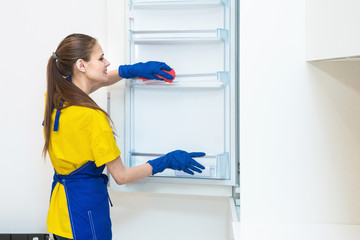 professional cleaning service. Two women in working uniform, in aprons, divide the cleaning of the kitchen of a private house, cottage. washing the refrigerator, tap, sink. Wash floor.