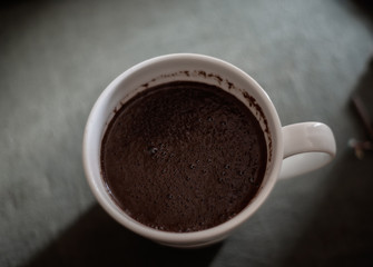 Cup of fresh coffee on dark blurred background, top view