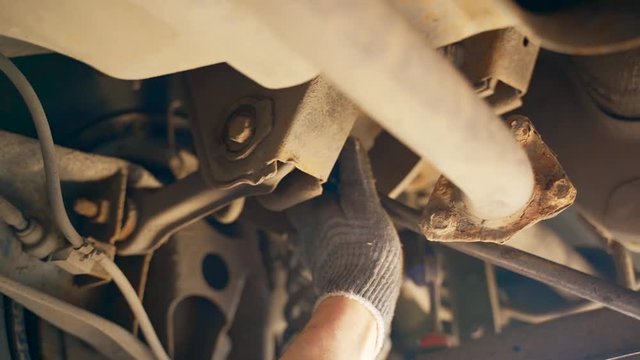 A car mechanic in the inspection pit unscrews the bolt on the car with a wrench. Adjustment of camber and toe.