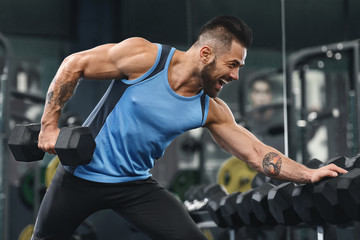 Fototapeta na wymiar Athlete lifting dumbbell, exercising at equipment rack in gym