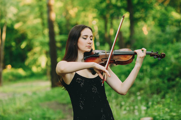 Beautiful girl in a black dress plays the violin in the woods