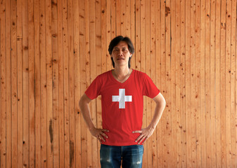 Man wearing Switzerland flag color shirt and standing with akimbo on the wooden wall background.