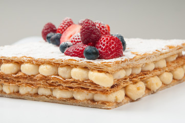 Close-up of crispy cake with berries and custard cream. Delirious fresh cake decorated powder sugar. Bakery shop concept