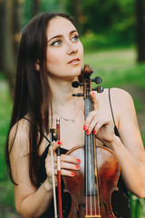beautiful girl holding a violin in her hands. violinist in the forest