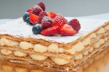 Close-up of puff pastry layer cake decorated with fresh berries. Custard cream between layers. Bakery concept