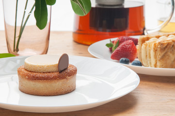 Closeup of cakes portions, berries, glass and teapot on table. Delicious pastries and teapot with tea on wooden table. Breakfast or dessert concept.