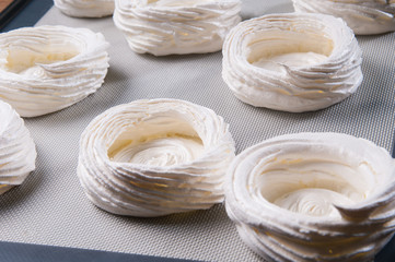 Closeup of meringue nests on tray before baking. Delicious cookies. Pastry cooking or confection concept.