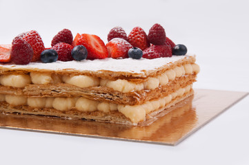 Close-up of sweet crispy cake with fresh berries. Puff pastry dessert on glowing carton. Food for party concept