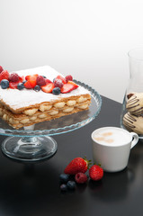 Fresh berry dessert on cake stand. Cappuccino and vase of cookies on table. Coffee shop concept