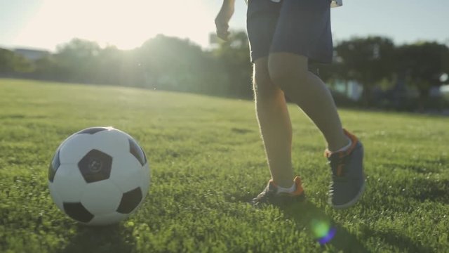 boy child training playing football in the park at sunset on a summer weekend vacation slow motion