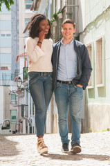 Happy Caucasian guy enjoying walk with his beautiful Afro American girlfriend. Mix raced couple walking city alley. Millennials concept