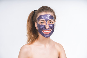 emotional portrait of a young beautiful european girl in violet cosmetic mask on her face. European, 22 years old, white, empty background