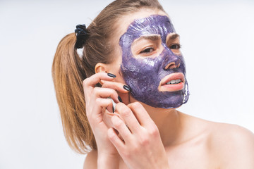 a young girl with a beautiful face with difficulty removes a purple cosmetic mask. Close-up. Macro. Pain, irritation. Facial care