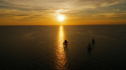 Naklejka na ściany i meble Sunset above the sea surface with sail boats, aerial view Boracay, Philippines. Reflected sun on a water surface. Sunset over ocean. Seascape, Summer and travel vacation concept