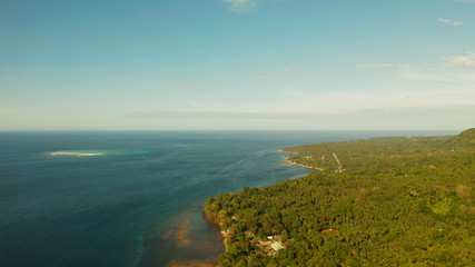 Seascape island coast with forest and palm trees, coral reef with turquoise water, aerial view. Coastline of tropical island covered with green forest against the blue sky with clouds and blue sea