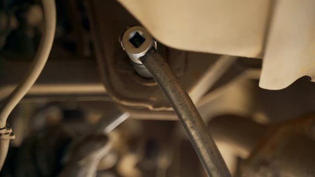 A car mechanic in the inspection pit unscrews the bolt on the car with a wrench. Adjustment of camber and toe. Car suspension repair.