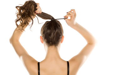 Young woman from behind,  tying her hair on white background