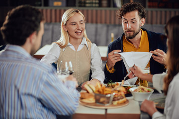Multiethnic friends sitting at restaurant, drinking alcohol, chatting and having burgers for dinner.