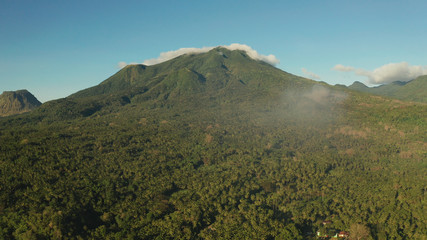 Mountains covered rainforest, trees and blue sky with clouds, aerial view. Camiguin, Philippines. Mountain landscape on tropical island with mountain peaks covered with forest. Slopes of mountains