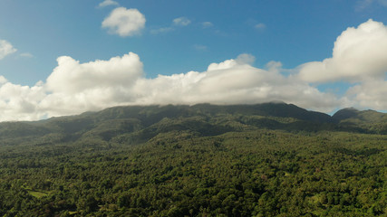 Fototapeta na wymiar Mountain landscape on tropical island with mountain peaks covered with forest from above. Mountains covered rainforest, trees and blue sky with clouds, aerial view. Camiguin, Philippines. Slopes of