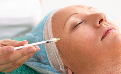 Gray hair woman in beauty clinic getting Botox injection to remove forehead wrinkles