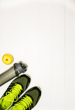 Fitness concept photo. Trainers, bottle of water and fruit apple are lying on white wooden table. Healthy lifestyle. Sport motivation background.