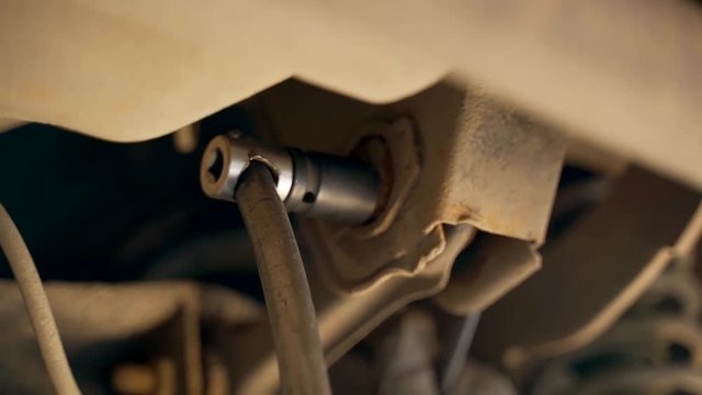 A car mechanic in the inspection pit unscrews the bolt on the car with a wrench. Adjustment of camber and toe. Car suspension repair.