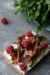 A nutritious and healthy breakfast: bread slice with aragula, raspberry, cream cheese and pastrami.