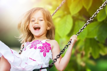 Little child blond girl having fun on a swing