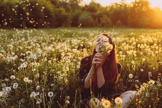 young woman with dandelions in hand in a field against the evening sun. sunset. joy. smile