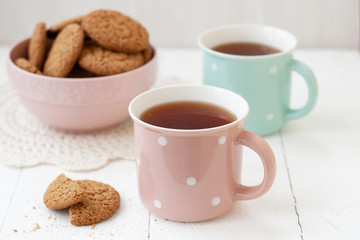 A tasty snack: two cups of tea and a bowl of cookies.