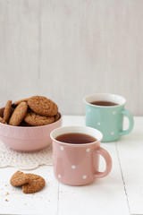 A tasty snack: two cups of tea and a bowl of cookies.