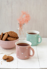 A tasty snack: two cups of tea and a bowl of cookies.